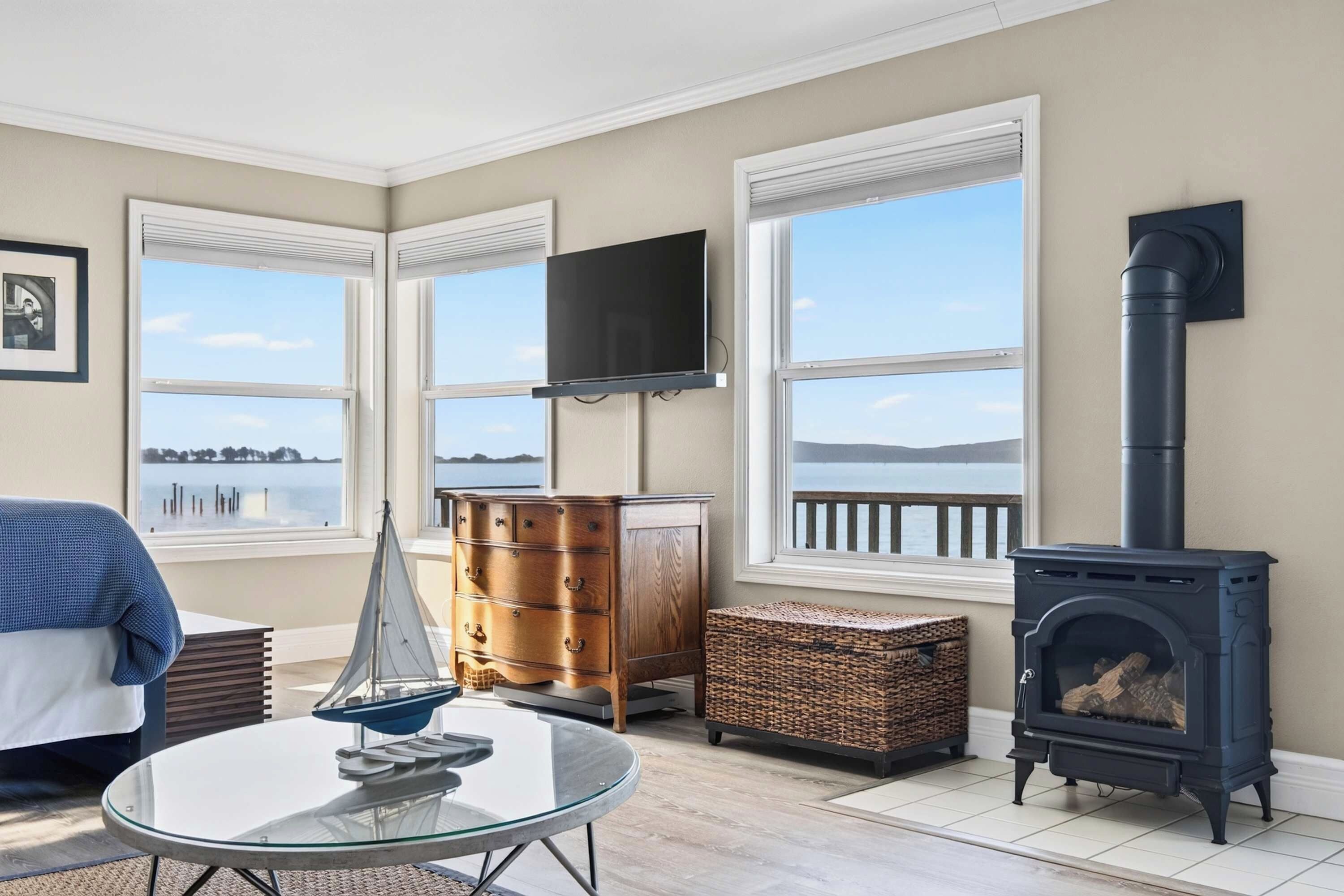 A living room with a view of a lake, a fireplace, a television, and a sailboat model.