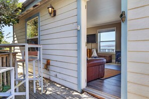 A wooden deck with a white railing, a brown leather bench, and a television mounted on the wall. - Bodega Bay waterfront studio cottage on stilts — 1 bed, gas fireplace (Bodega Bay)