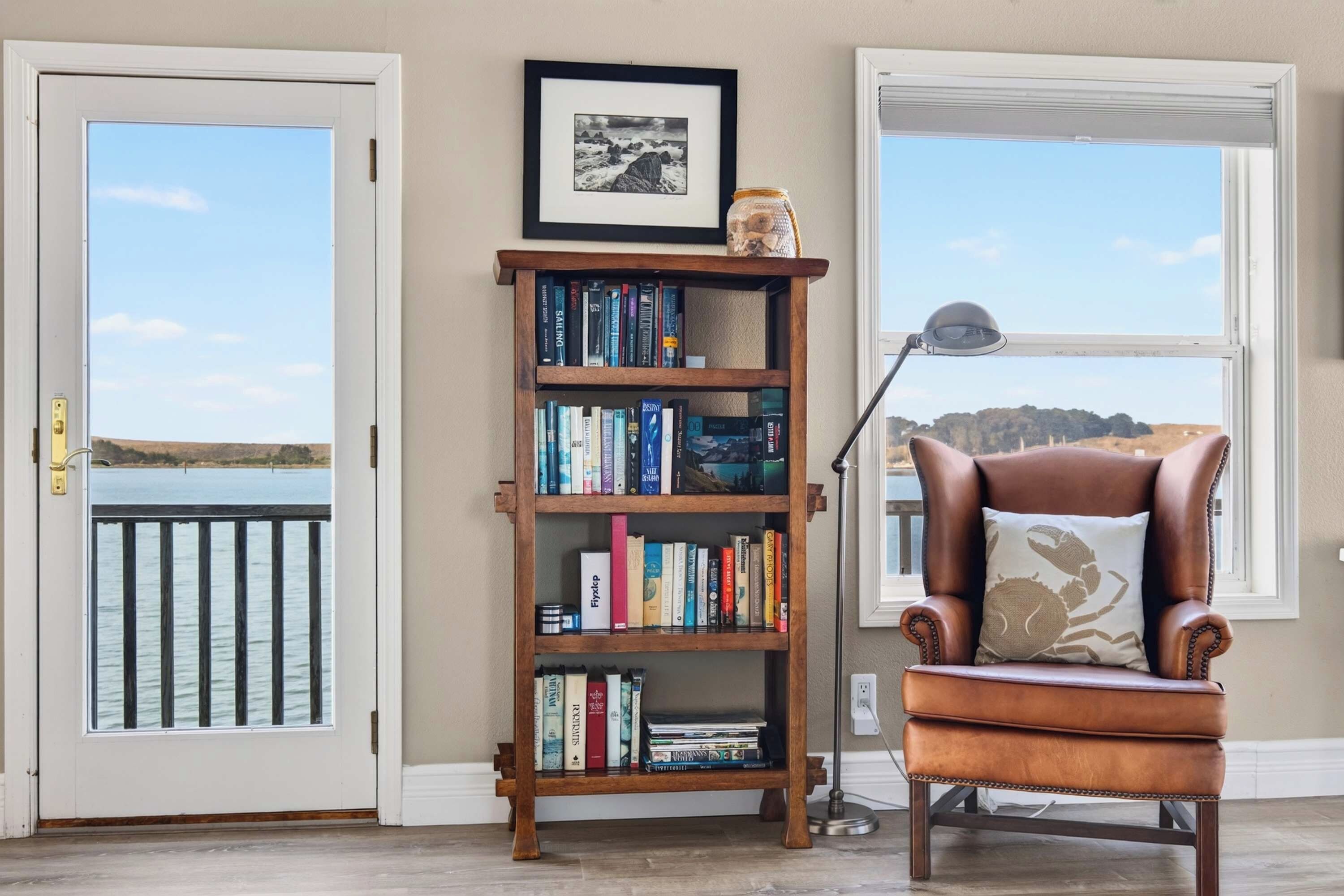 A room with a bookshelf, a leather armchair, and a view of the sea through a window.