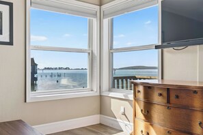 Una habitación con ventana saliente con vista a un cuerpo de agua, un aparador de madera y un cuadro en la pared.