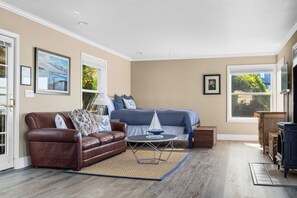 A room with a bed, a brown leather sofa, a small round table, and a blue sailboat model. - Bodega Bay waterfront studio cottage on stilts — 1 bed, gas fireplace (Bodega Bay)