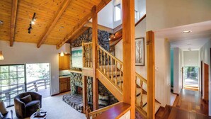 A spacious living area with a wooden staircase, stone wall, and large windows. - Wine Country Home w/ Solar-Heated Pool, Hot Tub & Mountain Views | Sleeps 8 (Santa Rosa)