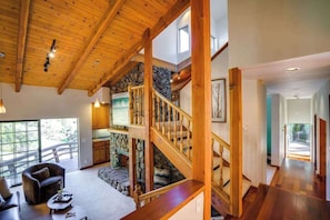 A spacious living area with a wooden staircase, stone wall, and large windows.