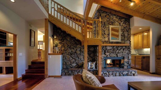 A spacious living area with a stone fireplace, wooden staircase, and a view of the kitchen. - Wine Country Home w/ Solar-Heated Pool, Hot Tub & Mountain Views | Sleeps 8 (Santa Rosa)