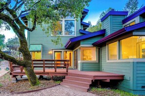 Une maison à deux étages avec un porche, un arbre et un banc.