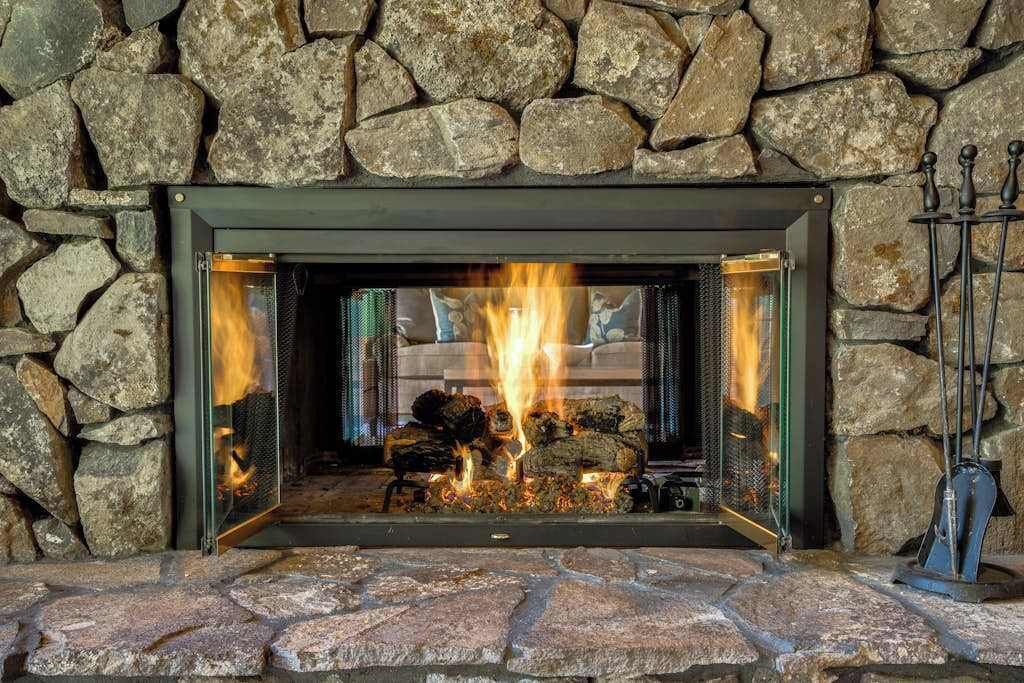 A stone fireplace with a fire burning inside, a metal grate, and a metal stand with a hook on the right side.