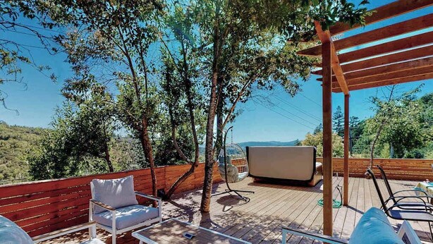 Eine Holzterrasse mit Sitzgelegenheiten, einem Fernseher und Blick auf die Landschaft.