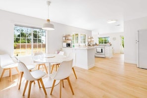 Una cocina moderna con armarios blancos, una isla central y un comedor con sillas blancas.
