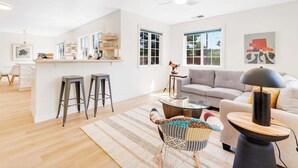 A modern living room with a sofa, a coffee table, and a dining area with stools. - Healdsburg 3BR vineyard farmhouse with game barn & wood fireplace (Healdsburg)