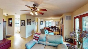 A spacious living room with a ceiling fan, a sofa, a red ottoman, and a dining area in the background. - Cloverdale 3BR hillside lodge on 7 acres with hot tub & wave pool (Cloverdale)