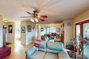 A spacious living room with a ceiling fan, a sofa, a red ottoman, and a dining area in the background. - Cloverdale 3BR hillside lodge on 7 acres with hot tub & wave pool (Cloverdale)
