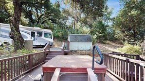 A wooden deck leading to a small building with a sign, surrounded by trees and a parked RV. - Cloverdale 3BR hillside lodge on 7 acres with hot tub & wave pool (Cloverdale)