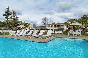 A swimming pool with lounge chairs and umbrellas, surrounded by buildings and trees.