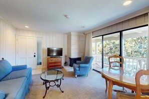 A living room with a sofa, a glass coffee table, a television, a fireplace, and a balcony with a view.