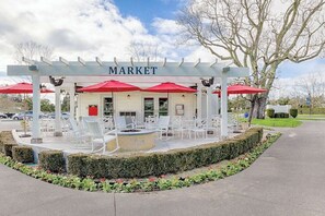 A covered outdoor seating area with a pergola, red umbrellas, and white chairs.