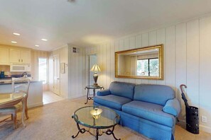 A living room with a blue sofa, a glass coffee table, a lamp, and a framed mirror on the wall.