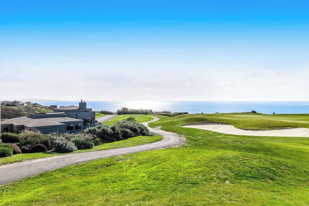 A golf course with a building, a winding road, and a view of the sea.