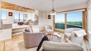 Een moderne woonkamer met een groot raam, een plafondventilator en uitzicht op het landschap.