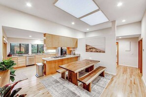 A modern kitchen with wooden cabinets, a large island, and a dining area with benches. - Bodega Bay 3BR ocean-view home overlooking The Links golf course (Bodega Bay)