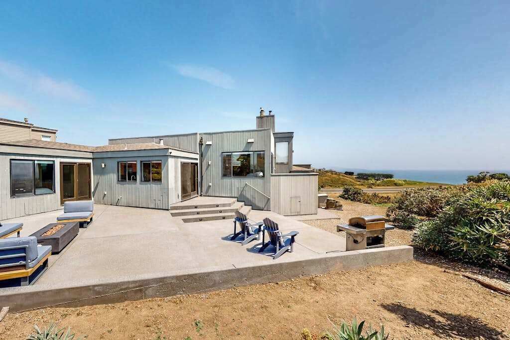 A modern house with a patio, outdoor seating, and a view of the ocean.