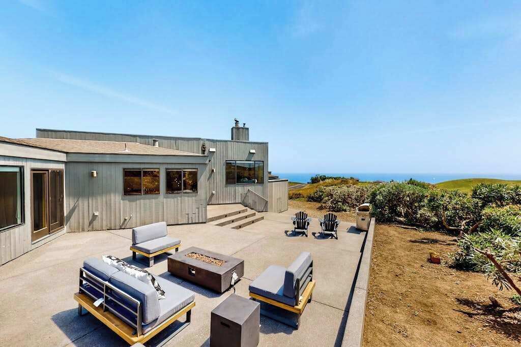 A modern house with a patio, outdoor seating, and a view of the ocean.