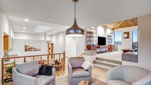 Een moderne woonkamer met grijze banken, een houten salontafel en een hangende hanglamp.