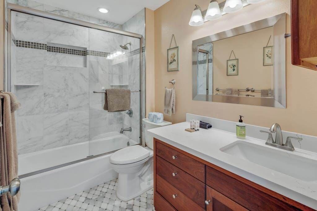 A bathroom with a glass-enclosed shower, a white toilet, a vanity with a mirror, and a sink.