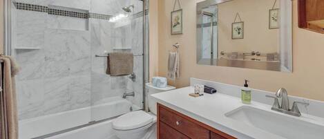 A bathroom with a glass-enclosed shower, a white toilet, a vanity with a mirror, and a sink.