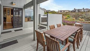 A wooden deck with a table and chairs, a glass door entrance, and a view of the surrounding landscape. - Bodega Harbour Ocean-View Hot Tub Retreat (Bodega Bay)