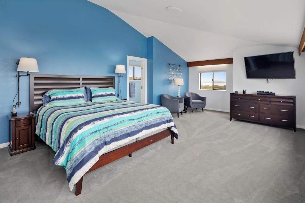 A bedroom with a bed, bedside tables, a desk, a chair, a dresser, and a TV.