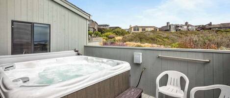 A hot tub on a deck with a railing, two chairs, and a view of houses in the background.