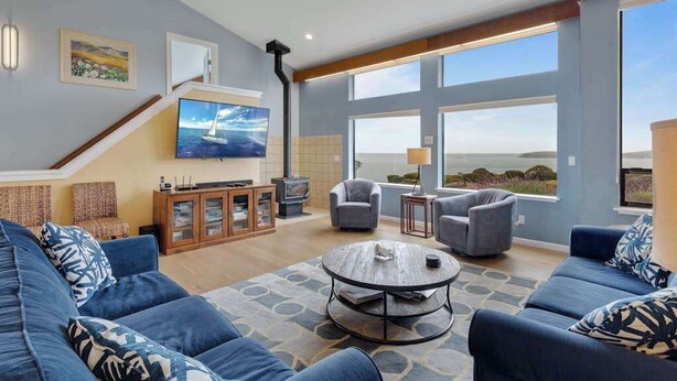 A spacious living room with a large window, a fireplace, and a television. - Bodega Harbour Ocean-View Hot Tub Retreat (Bodega Bay)
