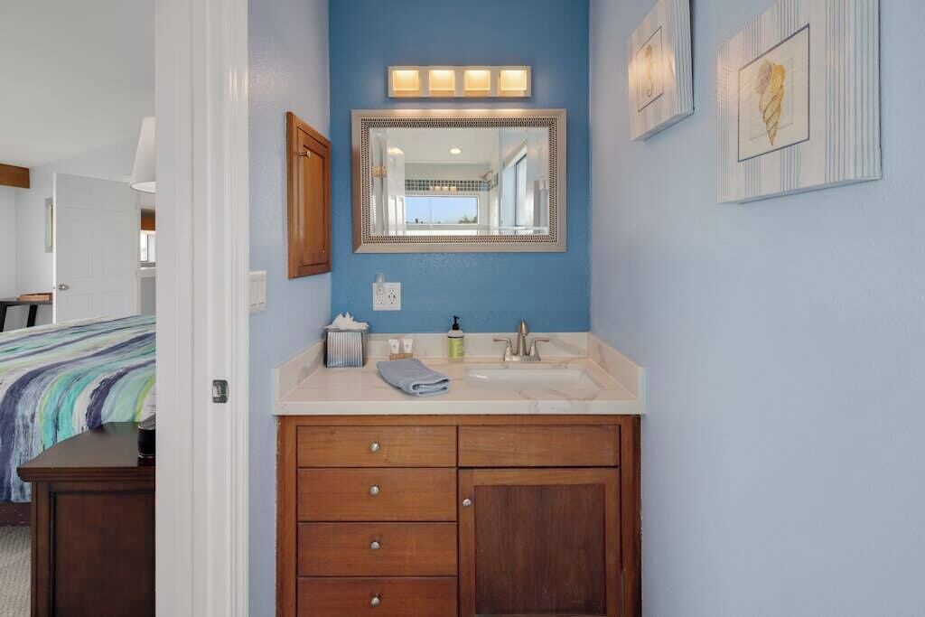 A bathroom with a blue wall, a wooden vanity with a sink, and a mirror above it.