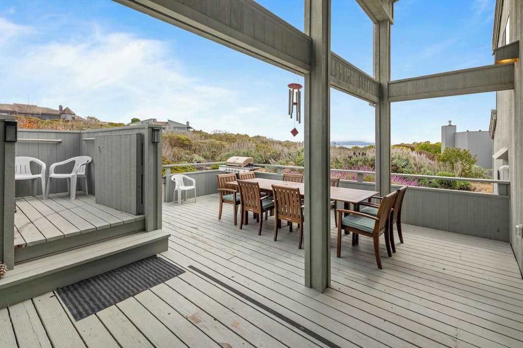 Un patio techado al aire libre con una mesa de comedor y sillas, una parrilla y vistas del paisaje.