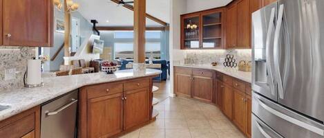 A modern kitchen with wooden cabinets, a stainless steel refrigerator, and a marble countertop.