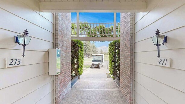 A gated driveway leading to a house with numbers 271 and 273 on the walls, a mailbox, and a vehicle parked in the background.