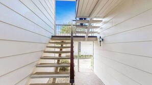 A spiral staircase with a metal handrail, leading to a balcony with a view of the outdoors.