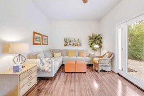 A living room with a sofa, ottoman, wooden floor, wall art, and a plant.