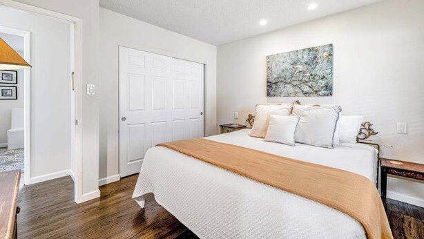 Une chambre à coucher avec un grand lit, une porte blanche, une table de chevet et une œuvre d’art accrochée au mur.