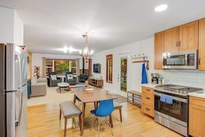 A modern kitchen with wooden cabinets, stainless steel appliances, and a dining area with blue chairs. - Cazadero 2BR creekside cabin — wraparound deck under the redwoods (Cazadero)