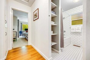 A hallway leading to a bedroom with a bed, a bathroom with a shower, and a tiled floor. - Cazadero 2BR creekside cabin — wraparound deck under the redwoods (Cazadero)