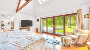 A bedroom with a large bed, a TV, a view of a garden through large sliding doors, and a skylight. - Sonoma 4BR wine country estate on 6 acres — pool, hot tub, sleeps 14 (Sebastopol)