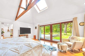 Un dormitorio con una cama grande, televisión, vistas a un jardín a través de puertas correderas y un tragaluz.