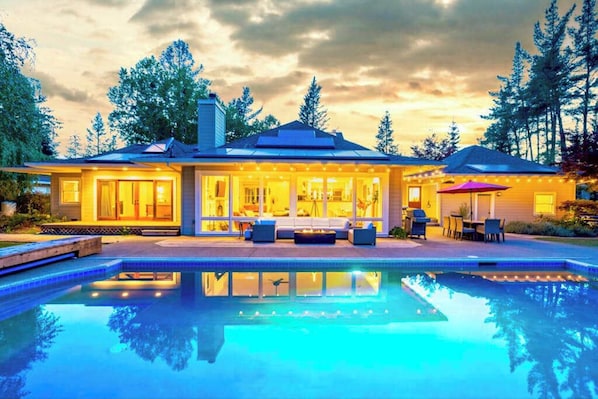 Una casa moderna con piscina, ventanas amplias y mobiliario de exterior.