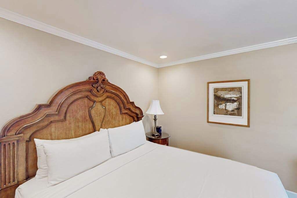 A hotel room with a large bed, a wooden headboard, a bedside table with a lamp, and a framed picture on the wall.