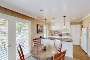 A kitchen with white cabinets, a dining table with chairs, and pendant lights. - Napa 1BR Silverado condo with two patios, fireplace & pool access (Napa)