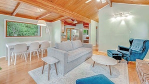 Un vaste espace de vie doté d’un plafond en bois, d’un canapé gris, d’un fauteuil bleu et d’une table à manger avec des chaises.