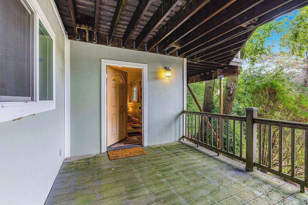 Une terrasse en bois avec une rambarde, une porte donnant sur un escalier intérieur et un luminaire fixé au mur.