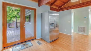 Une cuisine équipée d’un réfrigérateur en acier inoxydable, dotée d’un plancher en bois et offrant une vue sur une terrasse extérieure accessible par une porte-fenêtre coulissante.