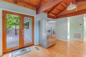 A kitchen with a stainless steel refrigerator, wooden flooring, and a view through a sliding glass door to an outdoor deck.